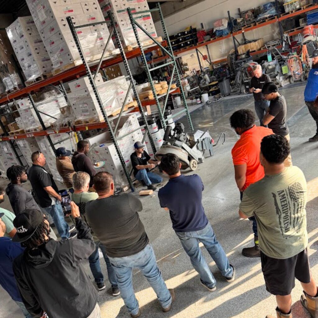 A group of people gathered in a warehouse listening to a speaker.