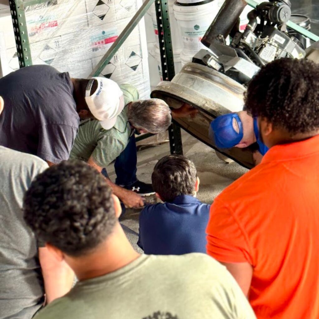 A group of people gathered around and looking at something on the ground indoors.