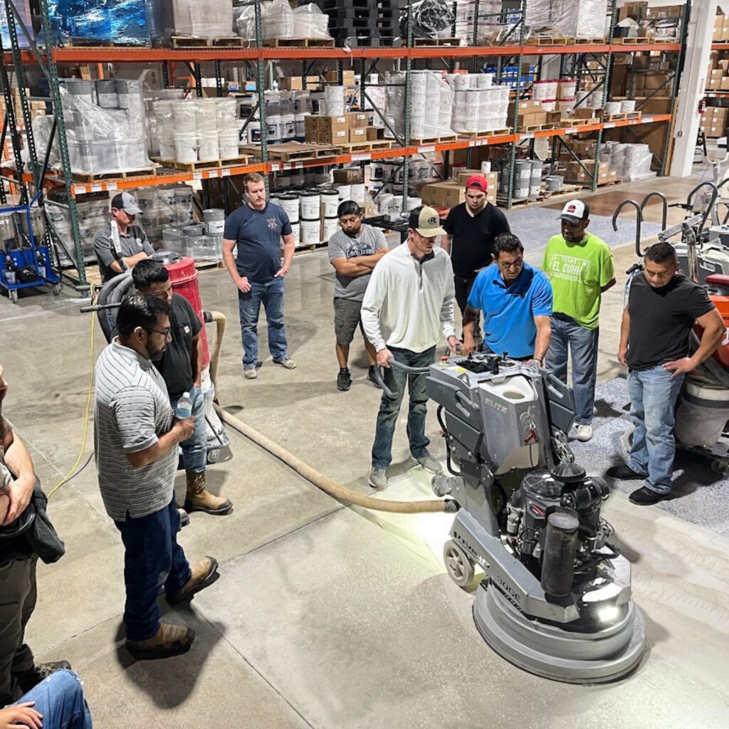 Group observing a floor polishing machine in a warehouse.