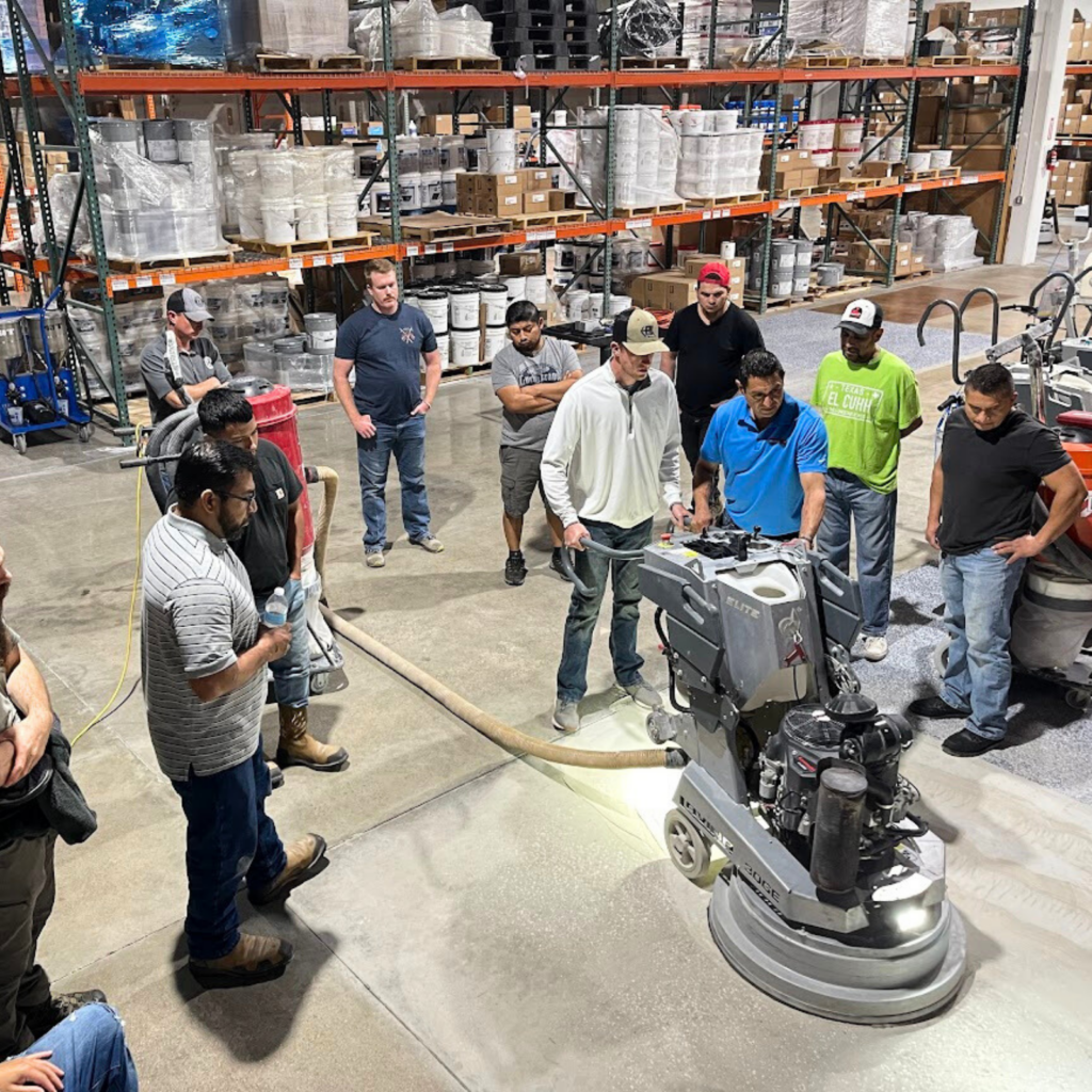 Group observing a floor polishing machine in a warehouse.